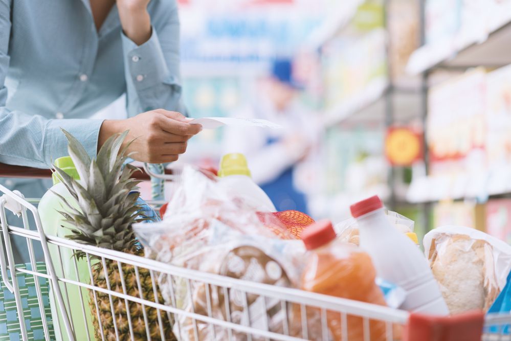 A woman pushing a grocery cart and holding a shopping list