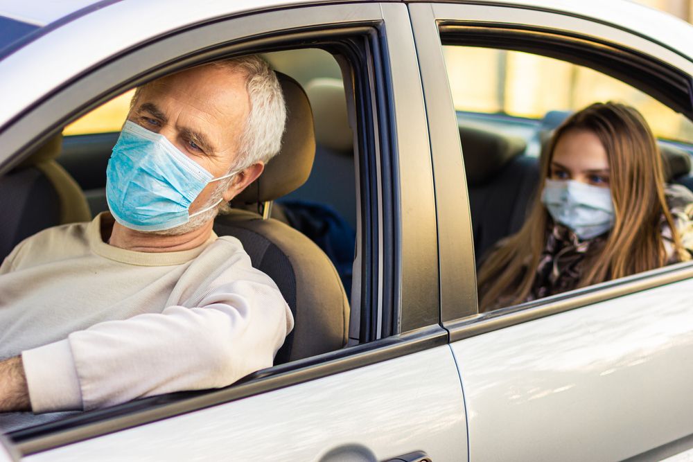 A senior man driving a car with a woman at the back seat