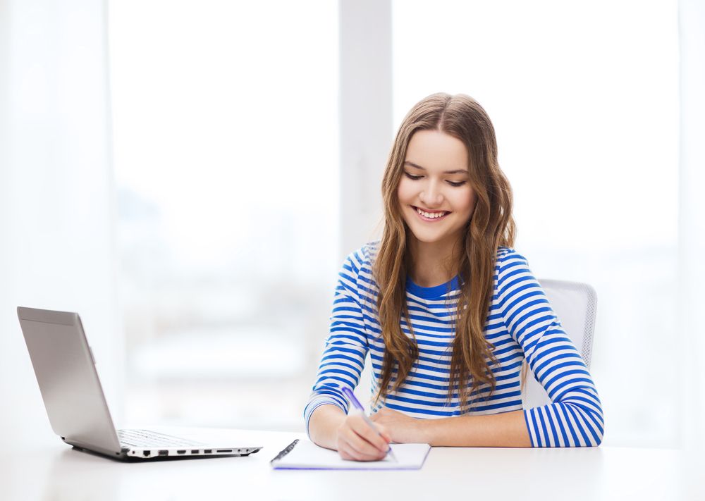 A young woman writing in front of her laptop
