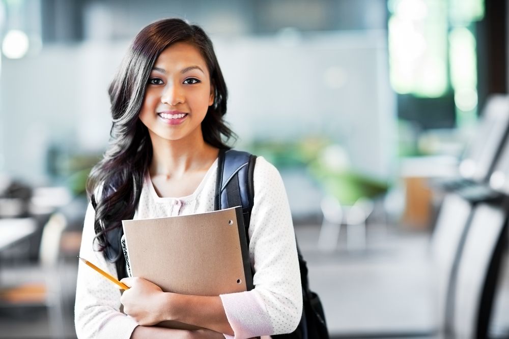 A young woman wearing a backpack and holding school supplies