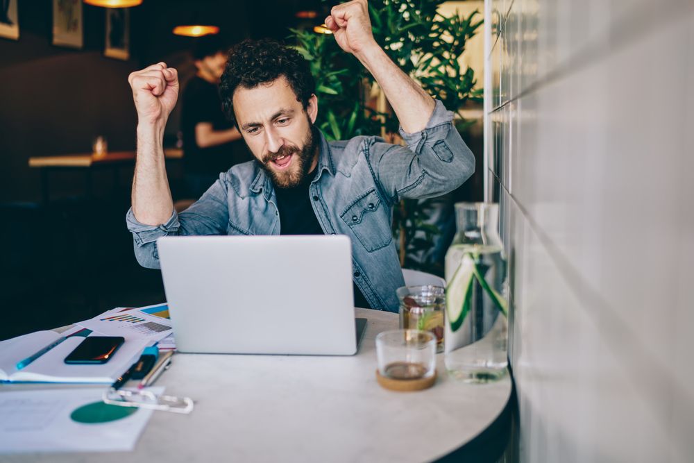 A man holding two fists while sitting in front of a laptop