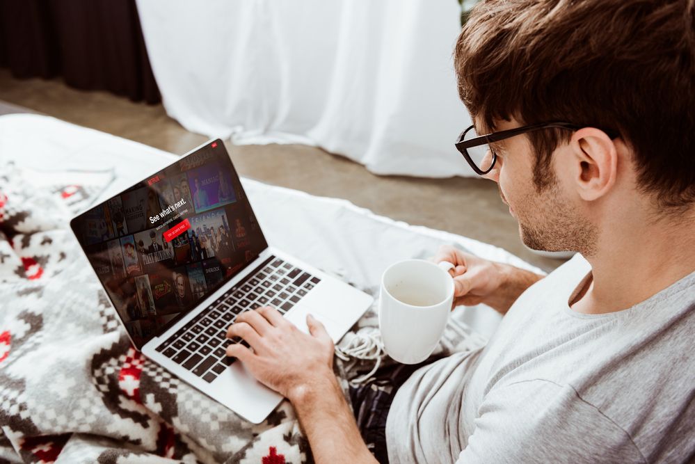 A man watching Netflix on his laptop in bed