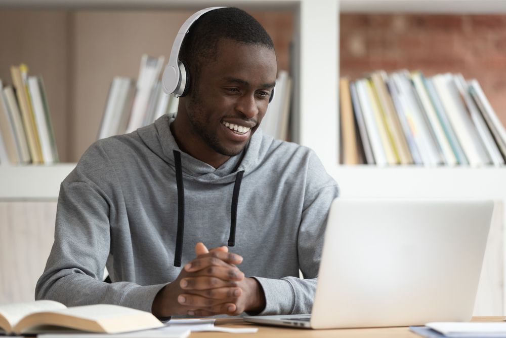 A young man wearing headphones and smiling to his laptop