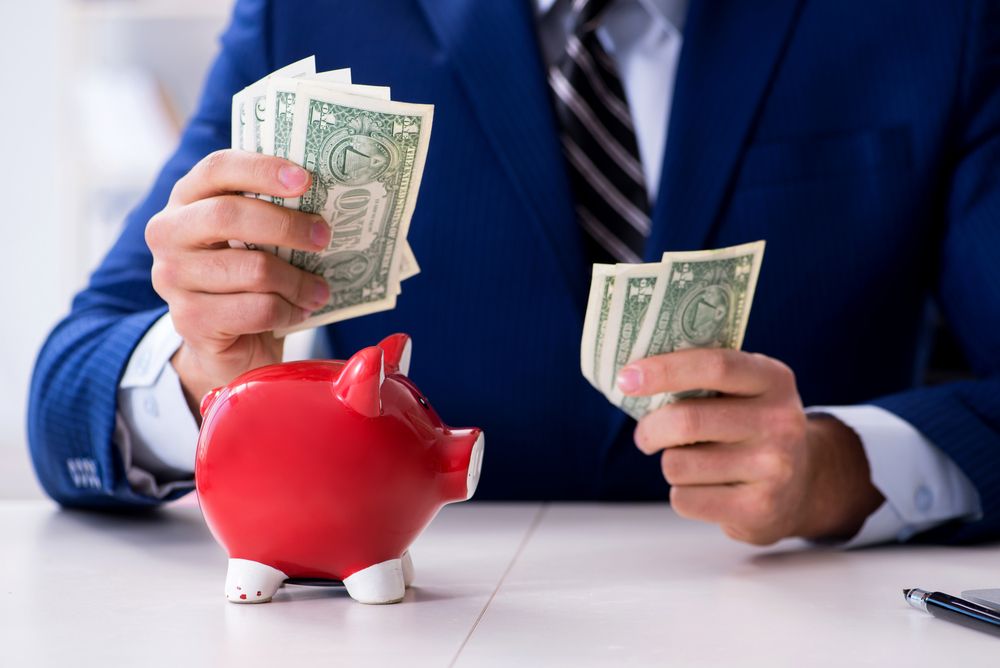 A man holding bills in front of a piggy bank