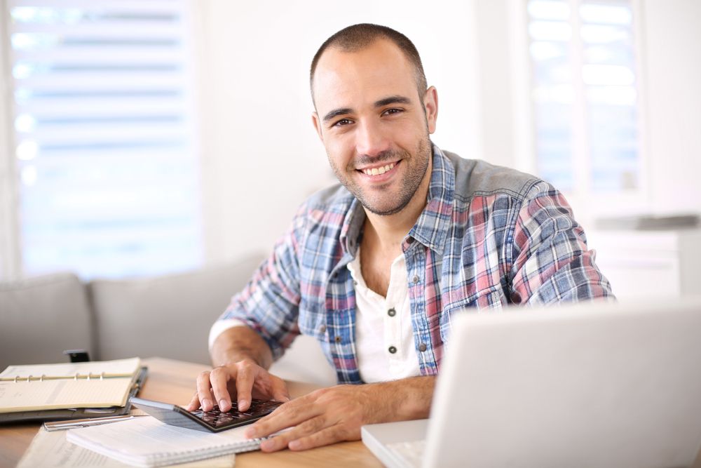 A man working with a calculator, laptop, and notebooks
