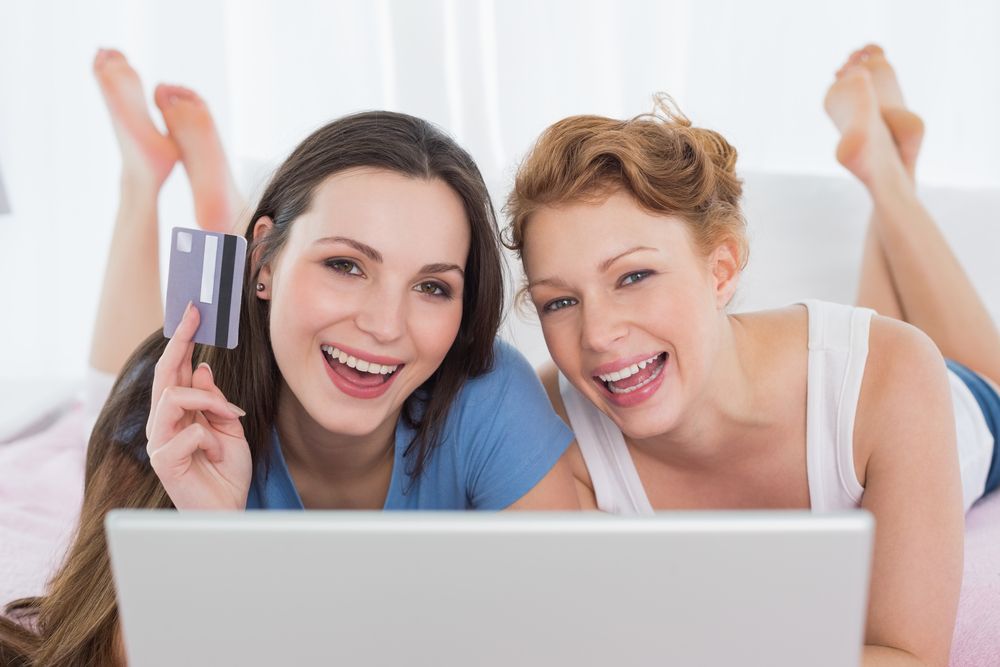Two women in bed with laptop and credit card