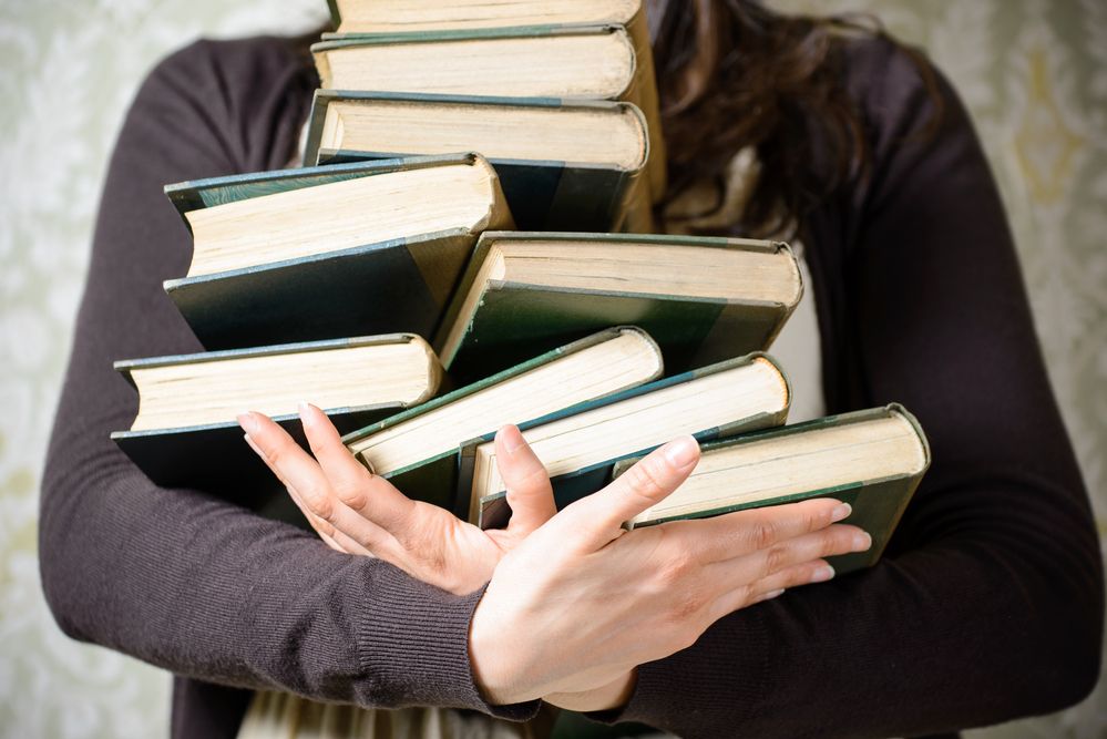 A young woman carrying a stack of books