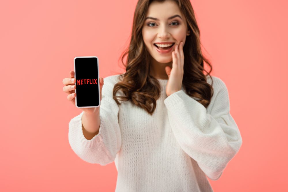 A woman holding a phone with Netflix flashed on screen