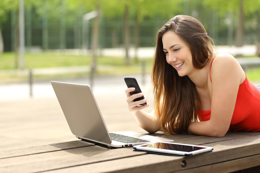 A woman using her laptop, tablet, and phone outdoors