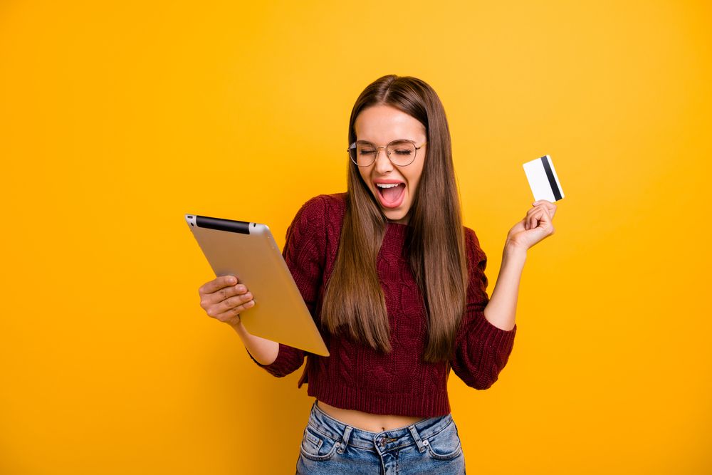 A young woman smiling and holding a tablet and a card
