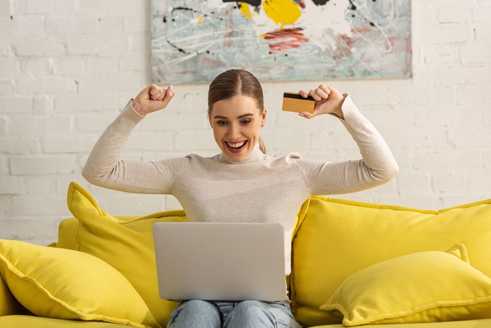 A woman with a credit card smiling to her laptop