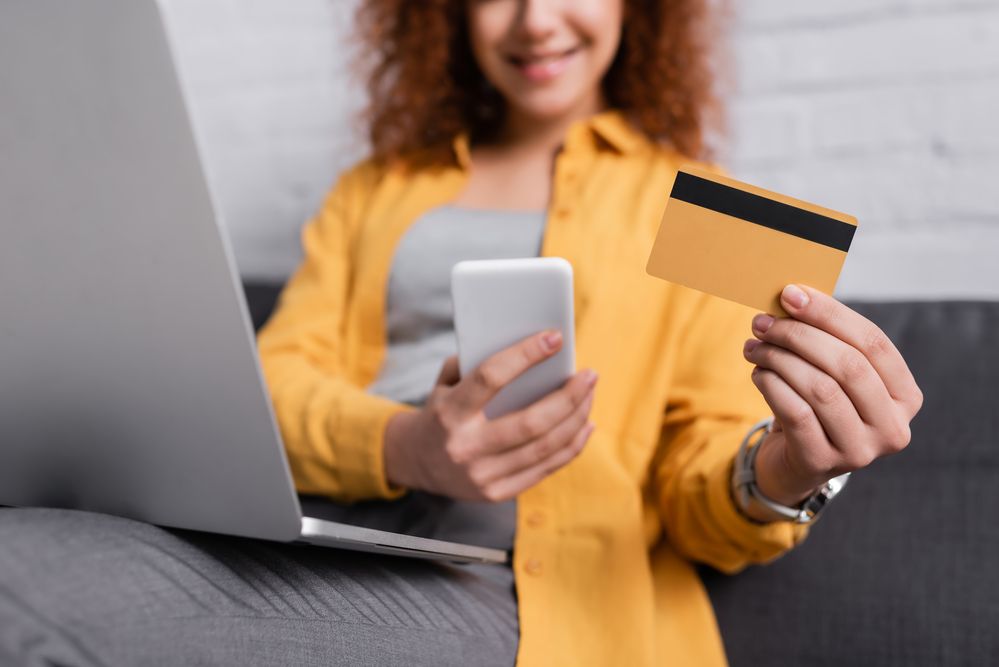 A woman holding a credit card, phone, and laptop