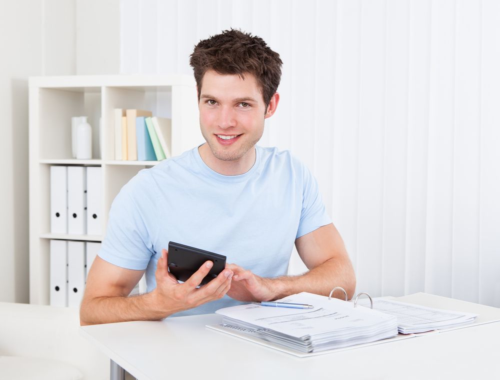 A young man holding a calculator over a binder