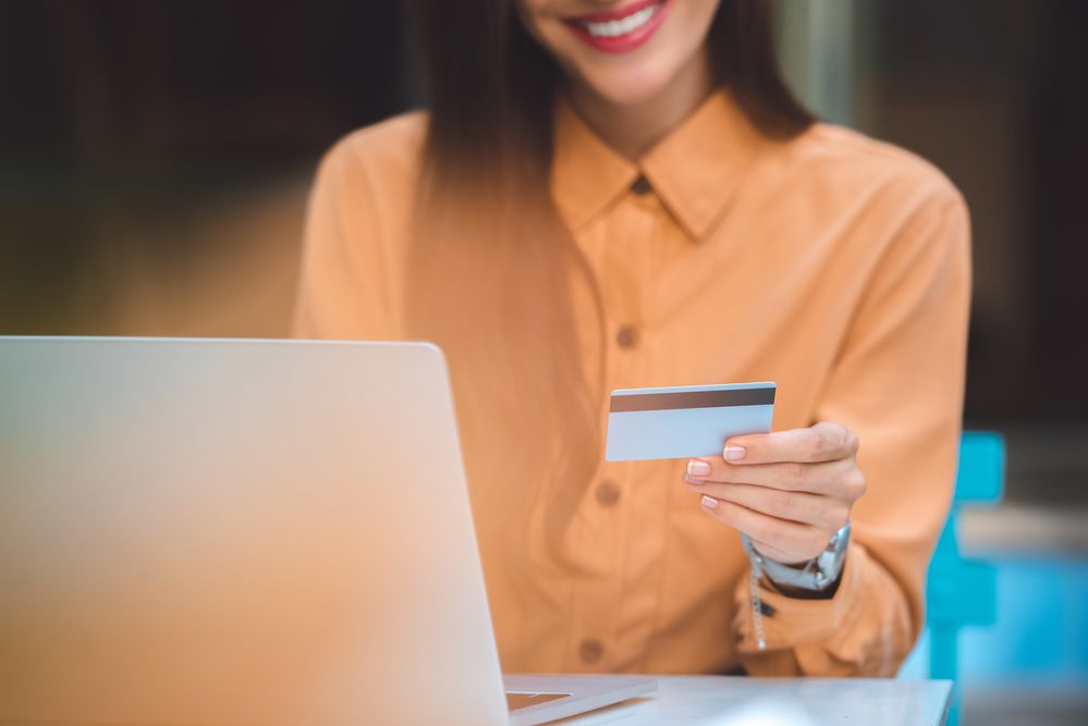 A young woman holding a credit card over her laptop