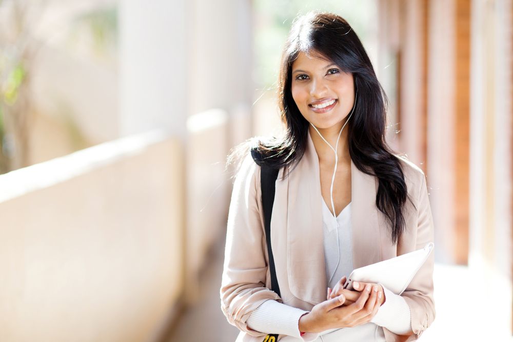 A young woman wearing earphones and carrying a tablet